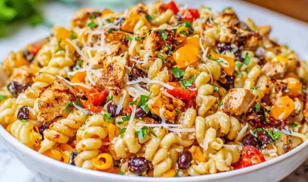 Large bowl of BBQ chicken pasta salad with shell pasta, black beans, red and orange bell peppers, corn, and cilantro tossed in creamy BBQ dressing