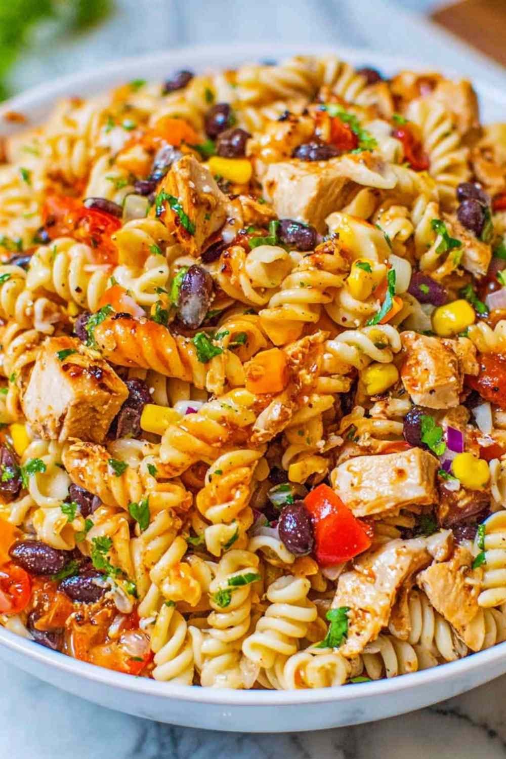 Large bowl of BBQ chicken pasta salad with shell pasta, black beans, red and orange bell peppers, corn, and cilantro tossed in creamy BBQ dressing