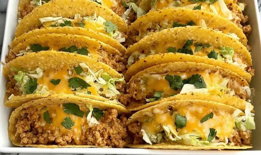 Baked ground chicken tacos in a 9x13 baking dish with crispy corn shells, melted cheese, and seasoned ground chicken filling