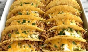 Baked ground chicken tacos in a 9x13 baking dish with crispy corn shells, melted cheese, and seasoned ground chicken filling