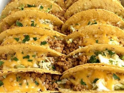 Baked ground chicken tacos in a 9x13 baking dish with crispy corn shells, melted cheese, and seasoned ground chicken filling