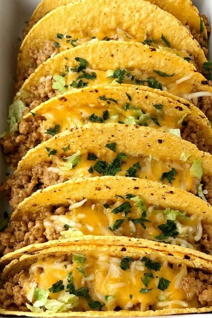 Baked ground chicken tacos in a 9x13 baking dish with crispy corn shells, melted cheese, and seasoned ground chicken filling