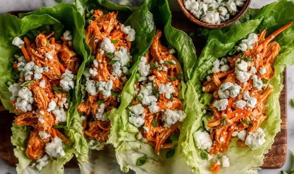 Buffalo chicken lettuce wraps arranged on a white serving platter with blue cheese crumbles, celery, red onion, and fresh parsley