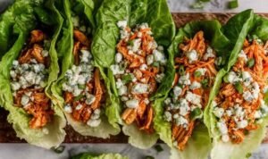 Buffalo Chicken Lettuce Wraps Buffalo chicken lettuce wraps arranged on a white serving platter with blue cheese crumbles, celery, red onion, and fresh parsley