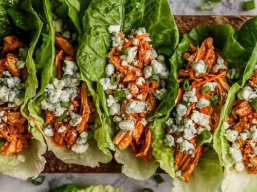 Buffalo chicken lettuce wraps arranged on a white serving platter with blue cheese crumbles, celery, red onion, and fresh parsley