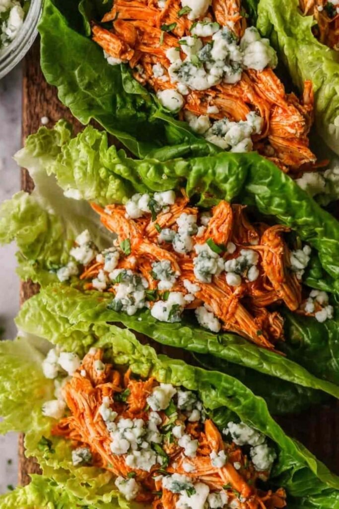 Buffalo chicken lettuce wraps arranged on a white serving platter with blue cheese crumbles, celery, red onion, and fresh parsley