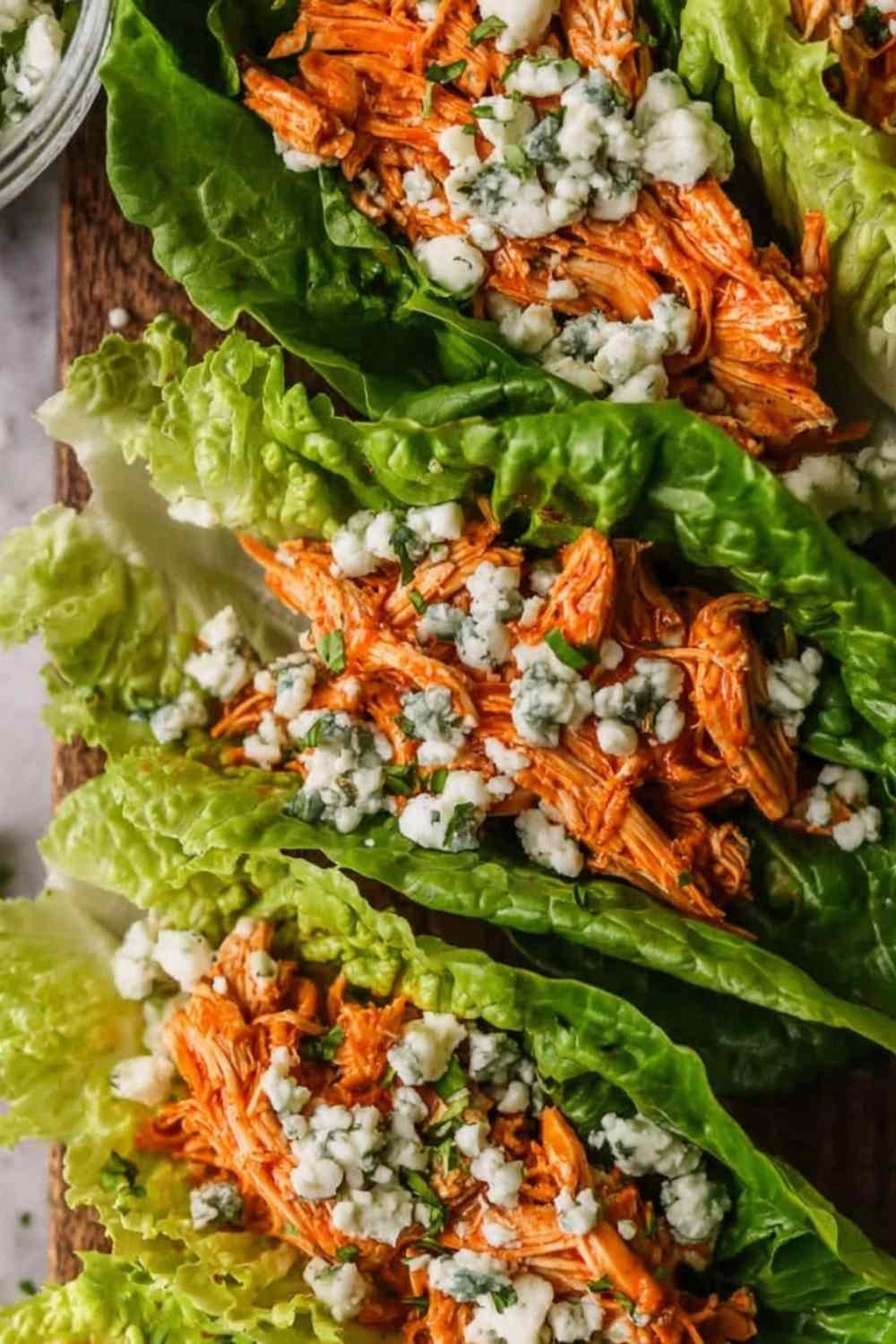 Buffalo chicken lettuce wraps arranged on a white serving platter with blue cheese crumbles, celery, red onion, and fresh parsley