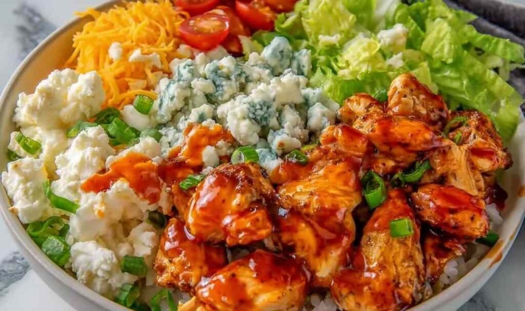 Buffalo Chicken Protein Bowl with saucy chicken over rice, cherry tomatoes, shredded cheddar, and ranch drizzle in a white bowl