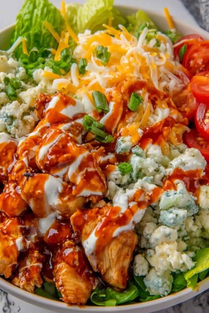 Buffalo Chicken Protein Bowl with saucy chicken over rice, cherry tomatoes, shredded cheddar, and ranch drizzle in a white bowl