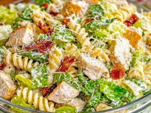 Chicken Caesar pasta salad with rotini, grilled chicken, turkey bacon, romaine, and shredded Parmesan in a white bowl