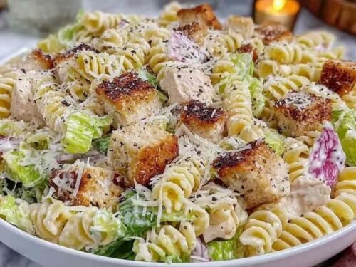 Creamy chicken Caesar pasta salad in a large white bowl with romaine, rotini, Parmesan, and garlic croutons