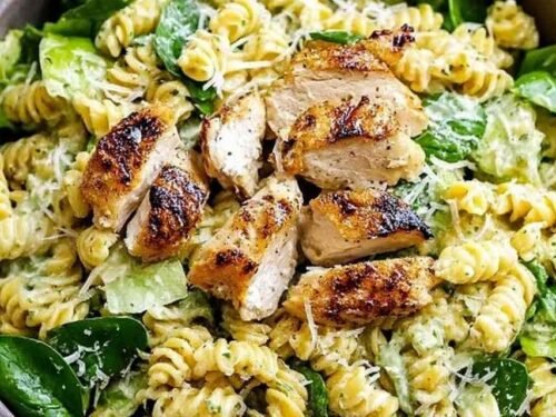 Large serving bowl of chicken Caesar pasta salad with rotini pasta, diced chicken, crisp romaine, cherry tomatoes, Parmesan, and croutons tossed in Caesar dressing