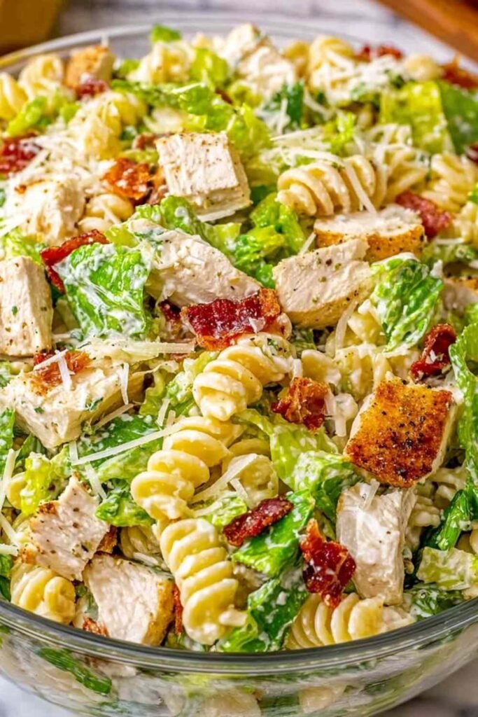 Chicken Caesar pasta salad with rotini, grilled chicken, turkey bacon, romaine, and shredded Parmesan in a white bowl