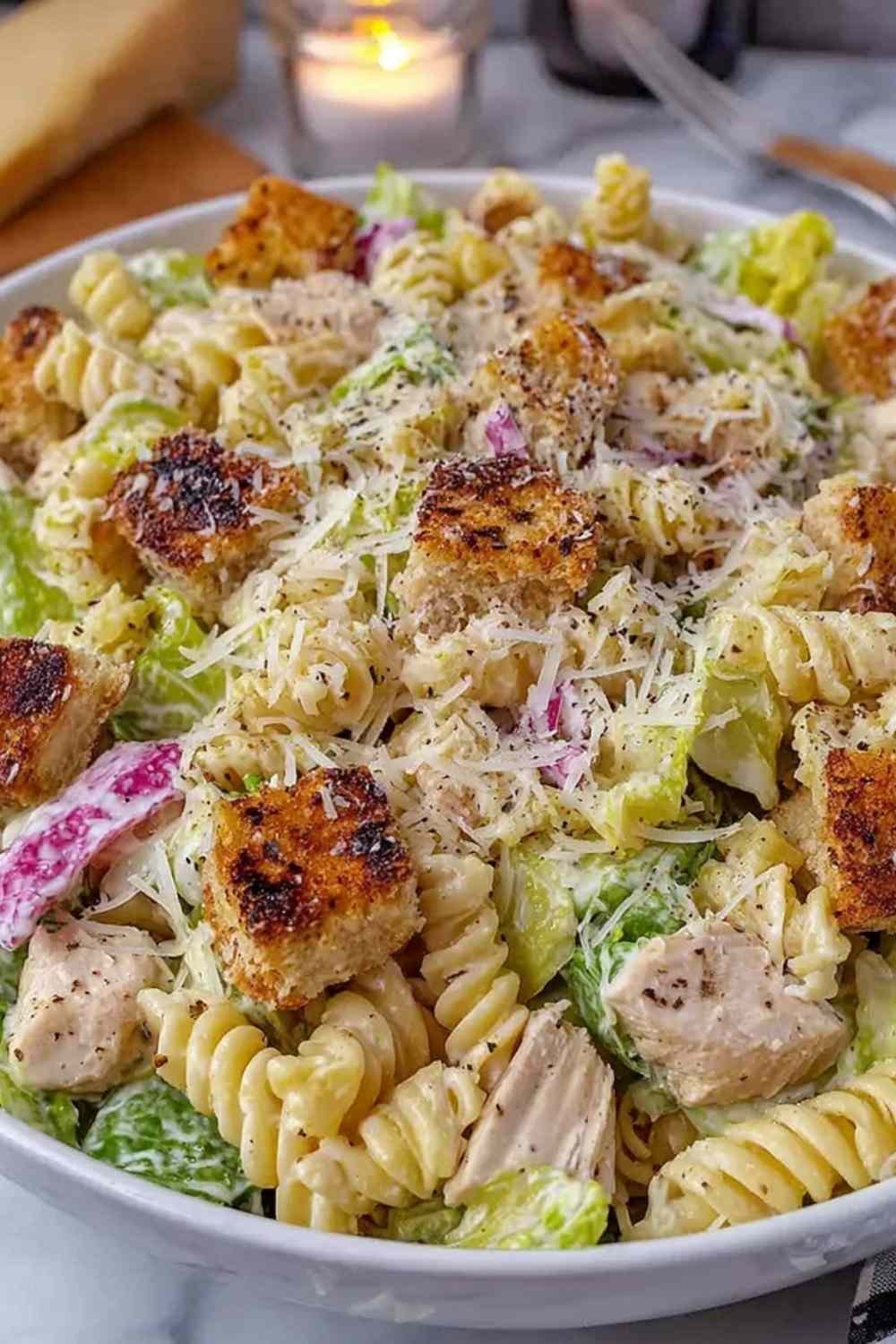 Creamy chicken Caesar pasta salad in a large white bowl with romaine, rotini, Parmesan, and garlic croutons