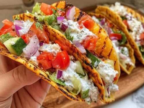 Chicken gyros smash tacos on a white plate topped with tzatziki, chopped cucumber, cherry tomatoes, red onion, and fresh cilantro