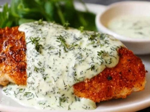 Chicken in basil cream sauce on a white plate with Parmesan cream sauce and fresh basil garnish