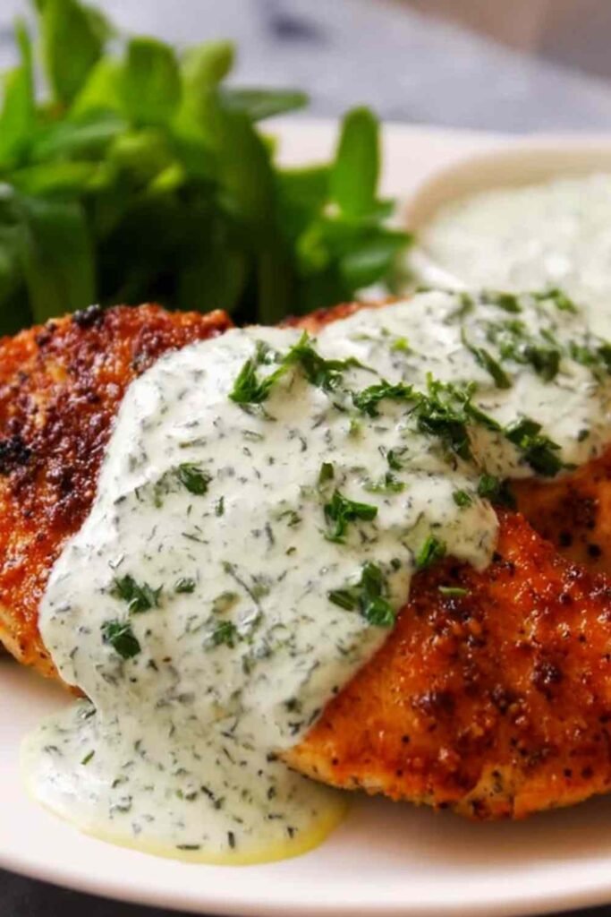 Chicken in basil cream sauce on a white plate with Parmesan cream sauce and fresh basil garnish