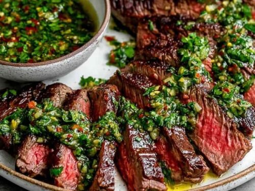 Chimichurri steak sliced against the grain on a wooden cutting board with vibrant green chimichurri sauce drizzled over the top