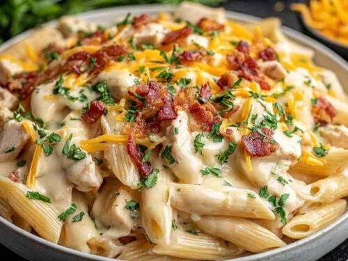 Creamy crack chicken penne in a pot with crispy bacon, shredded cheddar, and chopped green onions