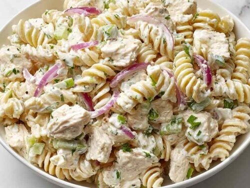Creamy chicken pasta salad with rotini, chopped chicken, celery, and red onion in a large white bowl
