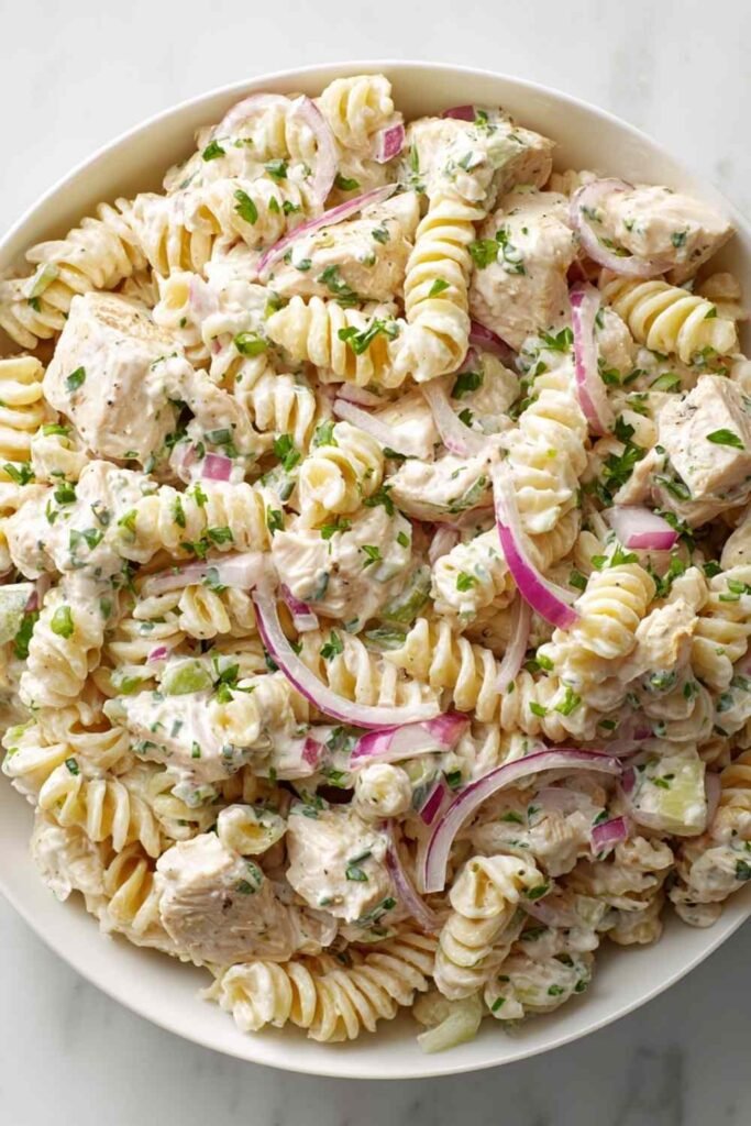 Creamy chicken pasta salad with rotini, chopped chicken, celery, and red onion in a large white bowl