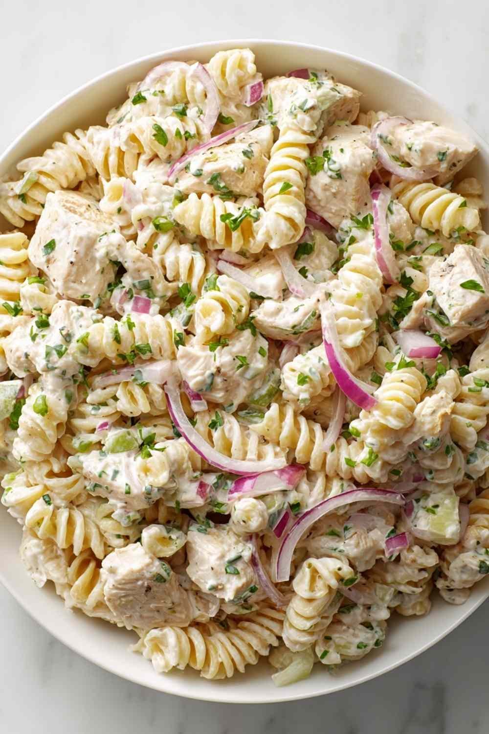 Creamy chicken pasta salad with rotini, chopped chicken, celery, and red onion in a large white bowl