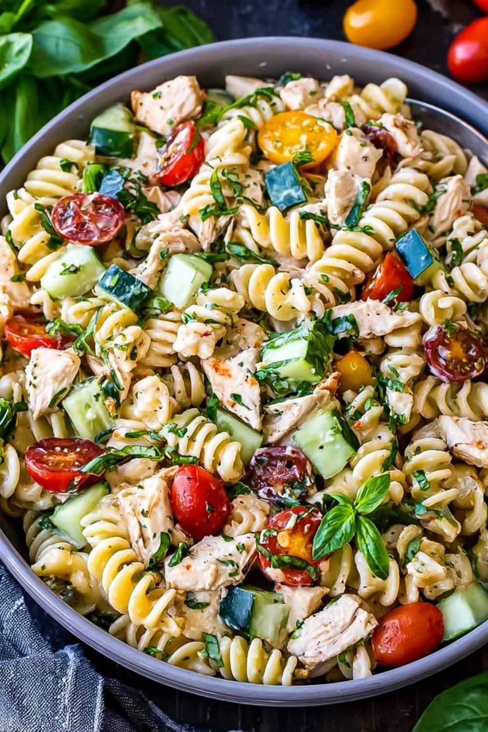 Creamy chicken pasta salad in large white bowl with avocado cherry tomatoes fresh basil grilled chicken and lemon garlic dressing