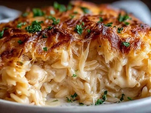 French Onion Chicken Orzo Casserole in a cast iron skillet with golden bubbly mozzarella on top, garnished with fresh thyme, straight from the oven