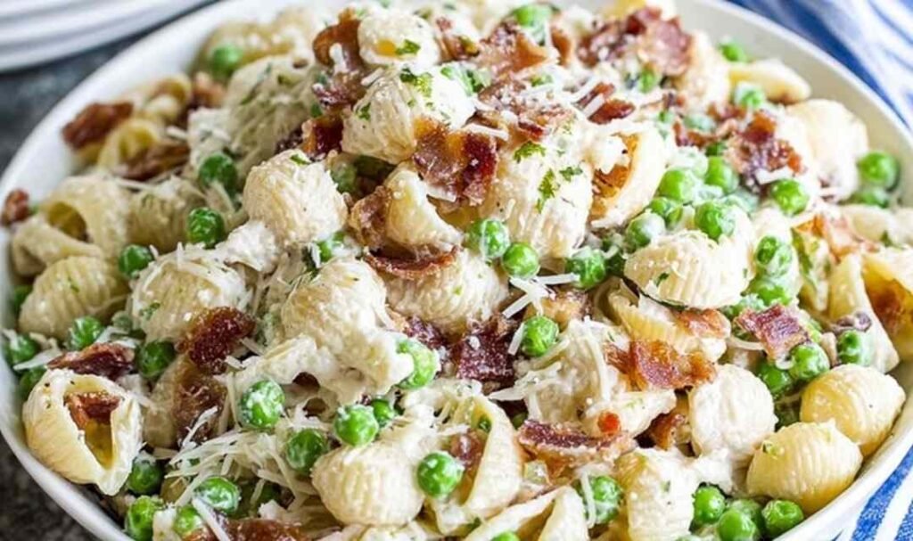 Creamy pasta salad in a white bowl with shell pasta, crispy bacon, peas, and Parmesan