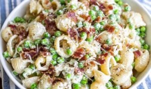 Creamy pasta salad in a white bowl with shell pasta, crispy bacon, peas, and Parmesan