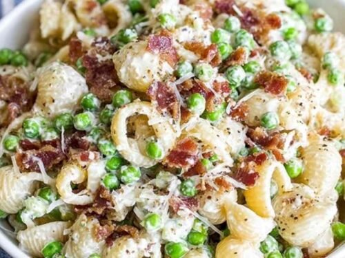 Creamy pasta salad in a white bowl with shell pasta, crispy bacon, peas, and Parmesan