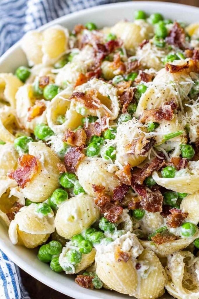Creamy pasta salad in a white bowl with shell pasta, crispy bacon, peas, and Parmesan