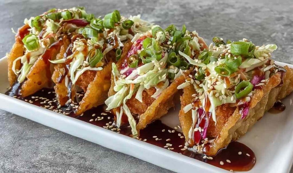 Crispy chicken wonton tacos with teriyaki glaze topped with shredded cabbage and sesame seeds on a white serving platter