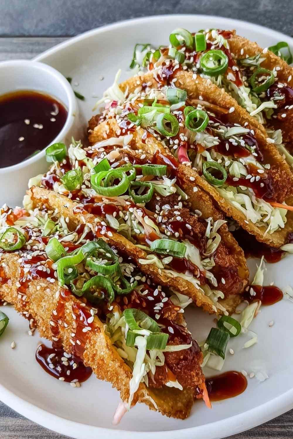 Crispy chicken wonton tacos with teriyaki glaze topped with shredded cabbage and sesame seeds on a white serving platter