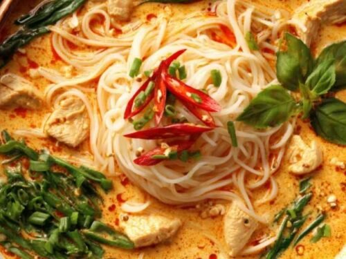 Damn Delicious Thai Red Curry Noodle Soup in a white bowl with fresh cilantro, basil, and a lime wedge garnish