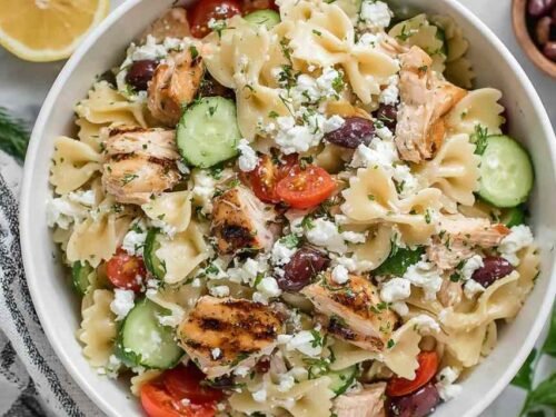 Overhead view of Greek Chicken Pasta Salad with bowtie pasta, cherry tomatoes, cucumber, olives, and feta in a white bowl