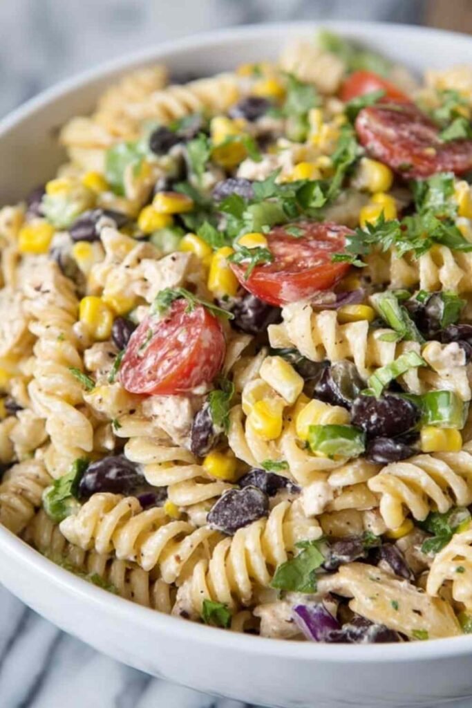 Large bowl of southwest pasta salad with rotini, grilled chicken, black beans, corn, tomatoes, and cilantro coated in chipotle ranch dressing
