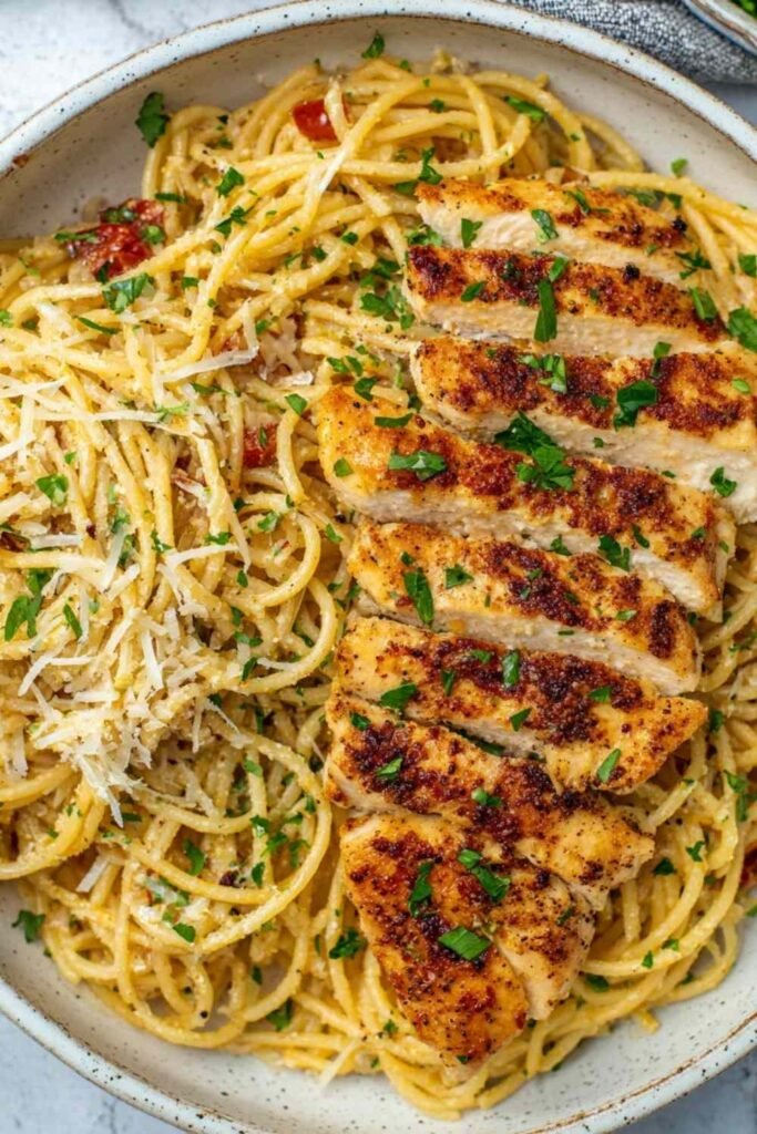 Garlic butter chicken pasta in a large skillet with sliced chicken breast, spaghetti, and Parmesan cheese garnished with fresh parsley