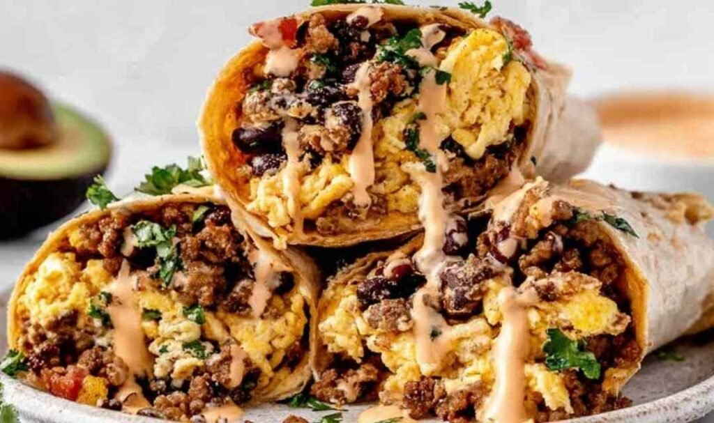 Six high protein breakfast burritos wrapped in foil on a wooden cutting board ready for meal prep