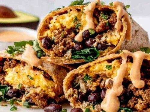 Six high protein breakfast burritos wrapped in foil on a wooden cutting board ready for meal prep