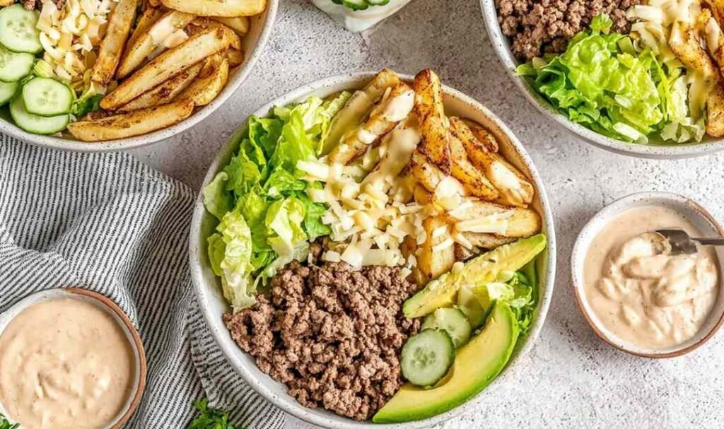 Burger bowl with seasoned ground beef, crispy potato chips, shredded lettuce, pickles, cheese, and homemade burger sauce