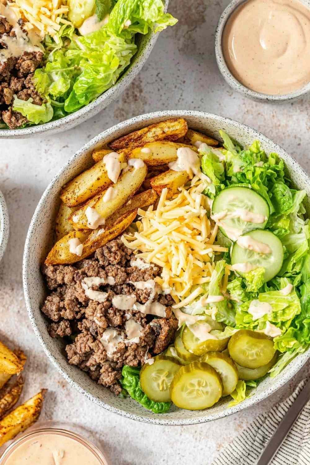 Burger bowl with seasoned ground beef, crispy potato chips, shredded lettuce, pickles, cheese, and homemade burger sauce