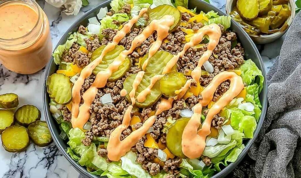 High protein cheeseburger bowl with seasoned ground beef, cheddar cheese, pickles, and creamy Big Mac sauce over chopped lettuce
