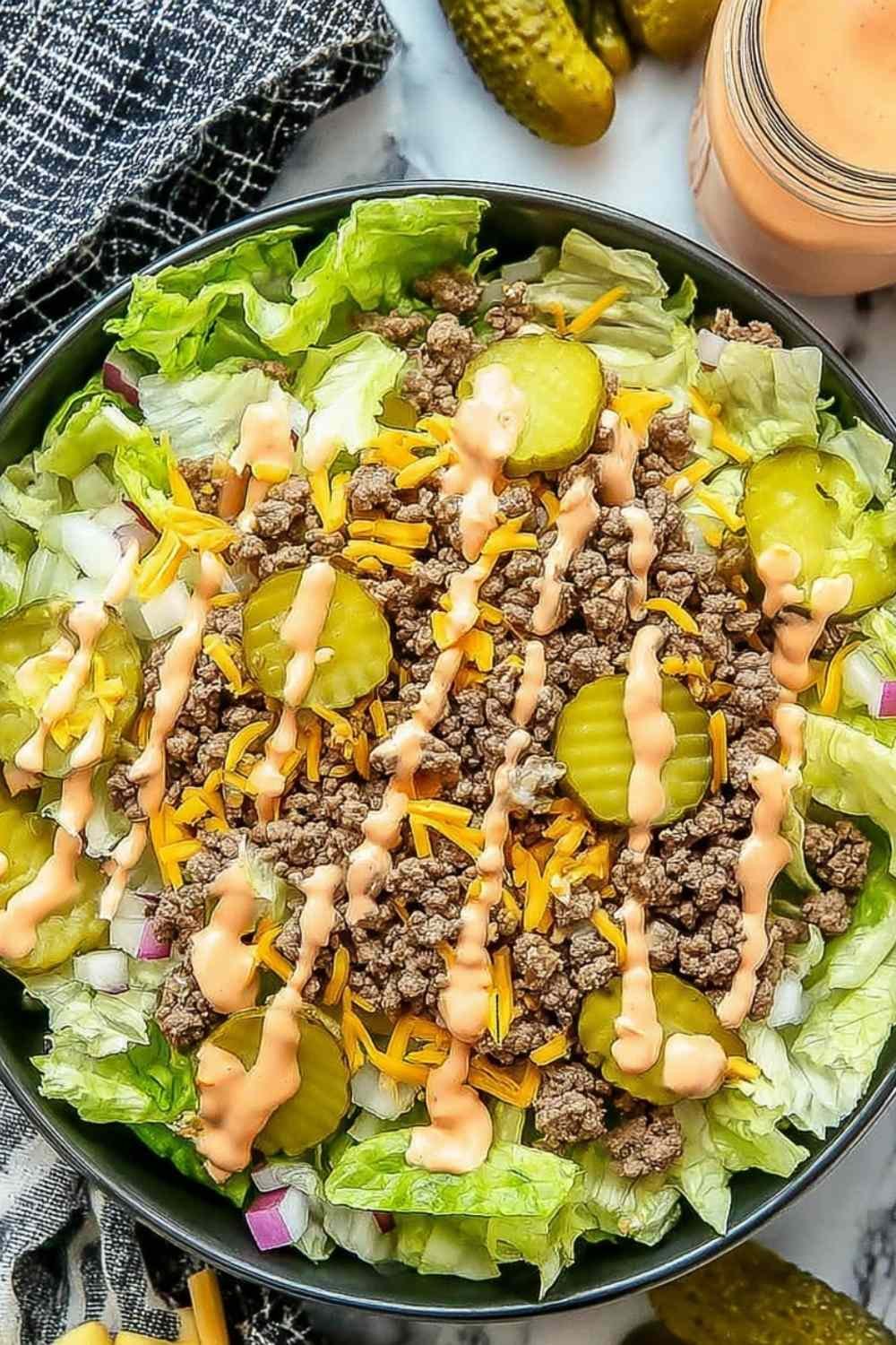 High protein cheeseburger bowl with seasoned ground beef, cheddar cheese, pickles, and creamy Big Mac sauce over chopped lettuce