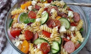 High protein Italian pasta salad with chickpea rotini, deli ham, turkey pepperoni, salami, feta, provolone, and fresh vegetables in a large white serving bowl