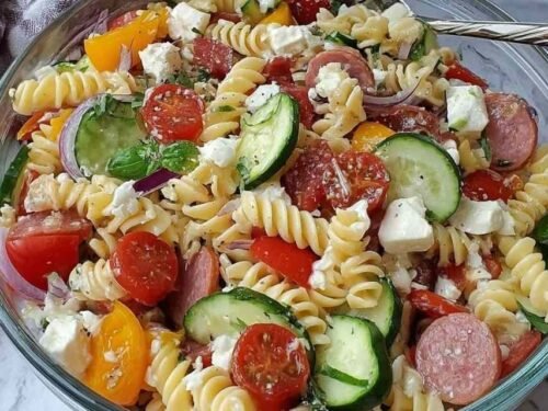 High protein Italian pasta salad with chickpea rotini, deli ham, turkey pepperoni, salami, feta, provolone, and fresh vegetables in a large white serving bowl