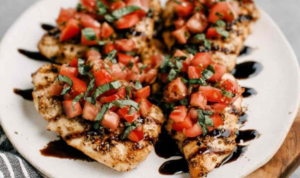 Bruschetta Chicken breasts on a white serving platter topped with fresh tomato basil topping and drizzled with balsamic glaze