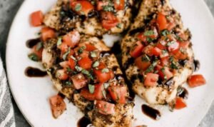 Bruschetta Chicken Bruschetta Chicken breasts on a white serving platter topped with fresh tomato basil topping and drizzled with balsamic glaze