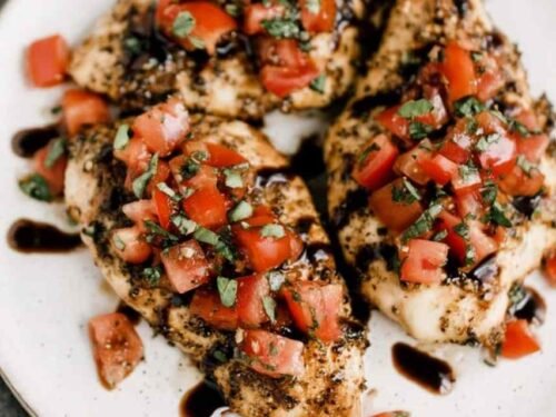 Bruschetta Chicken breasts on a white serving platter topped with fresh tomato basil topping and drizzled with balsamic glaze