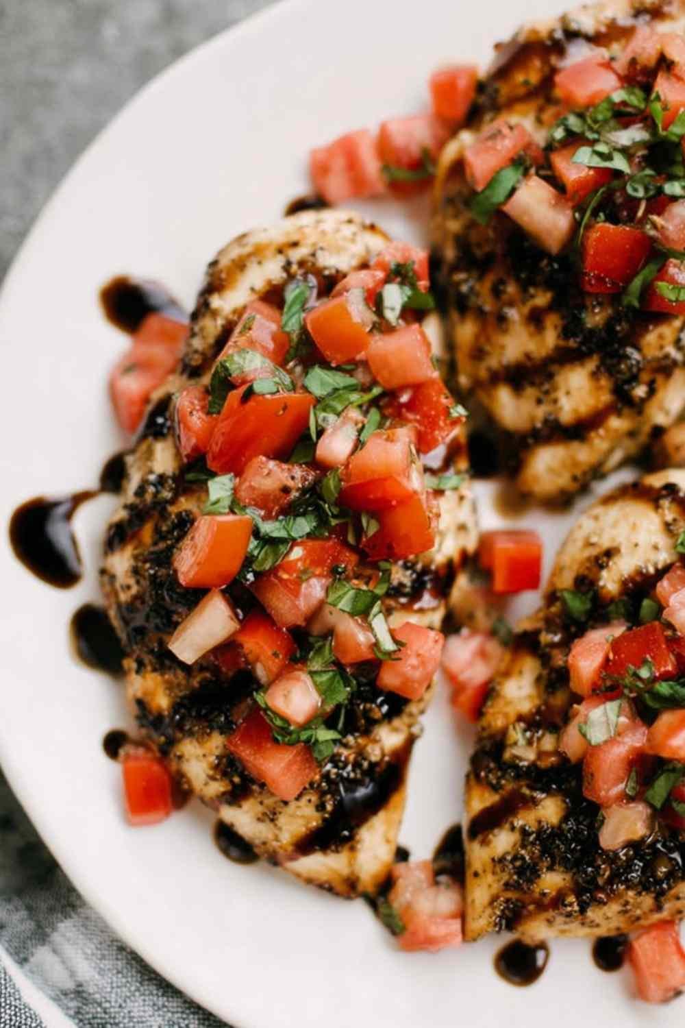 Bruschetta Chicken breasts on a white serving platter topped with fresh tomato basil topping and drizzled with balsamic glaze